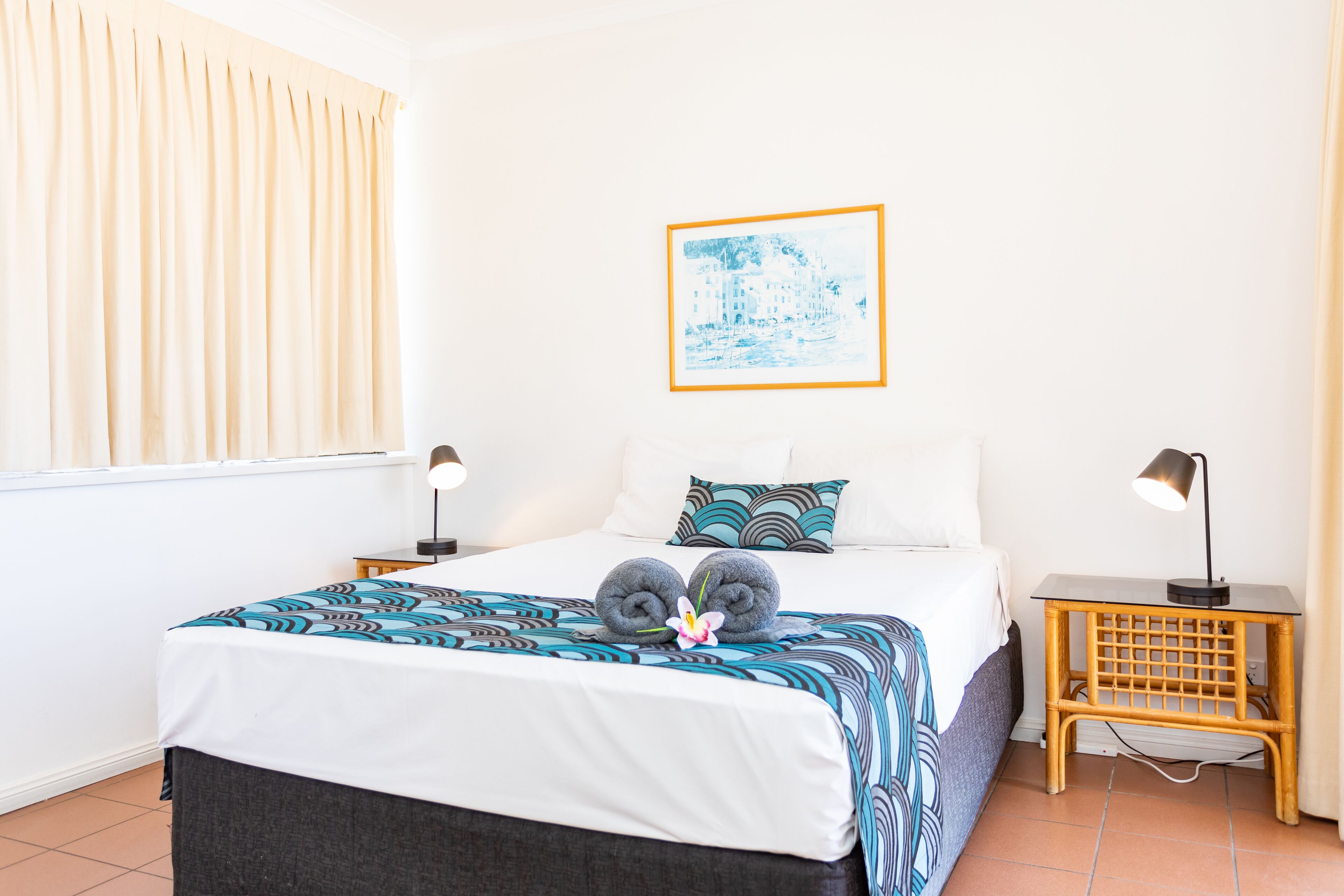 A neatly made bed with a patterned bedspread, two pillows, and a framed picture on the wall.