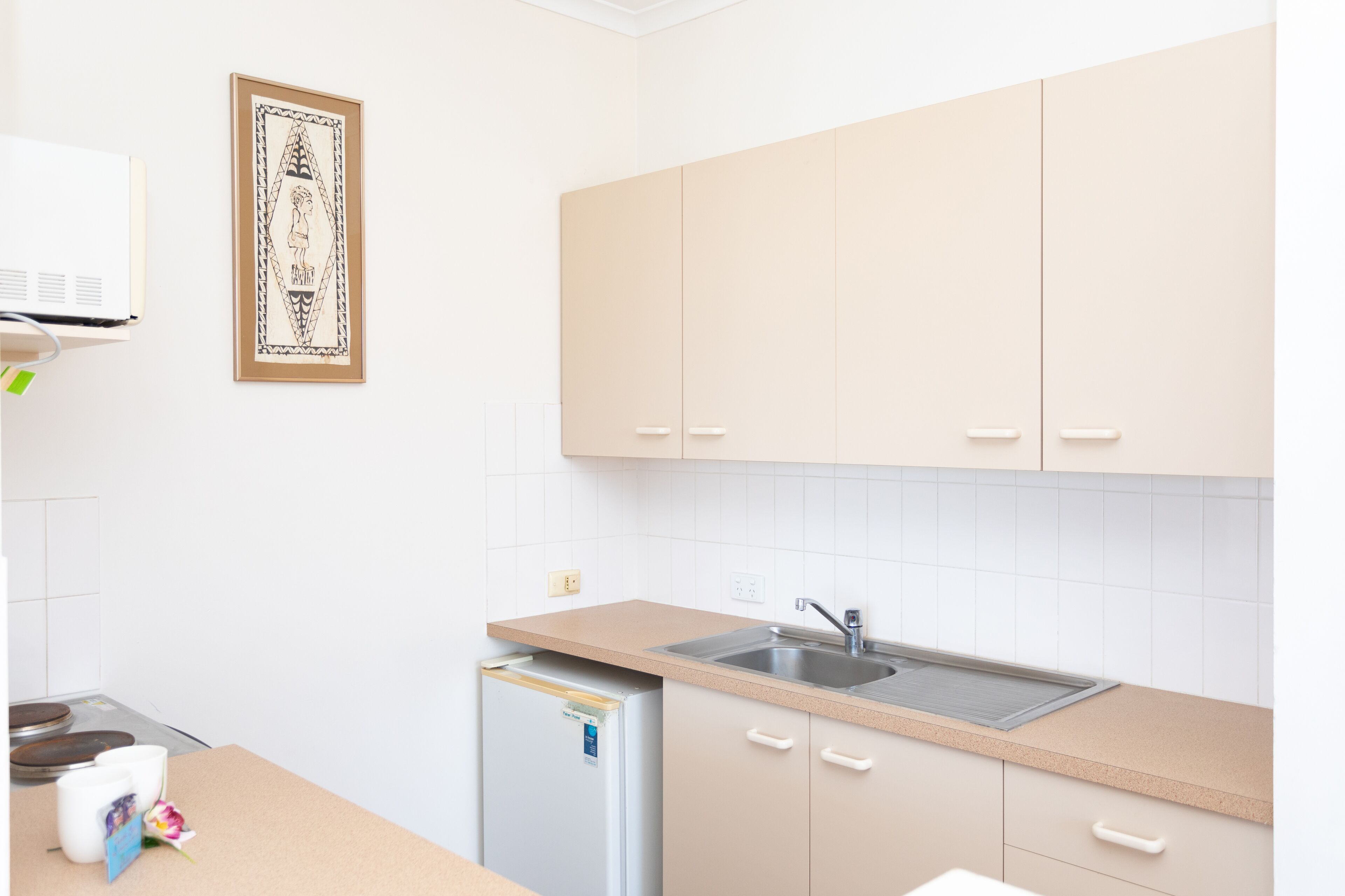 A kitchen with beige cabinets, a stainless steel sink, and a small refrigerator.