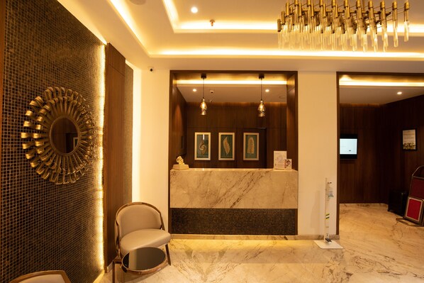 A hotel reception area with a marble counter, a large mirror, and a chandelier.
