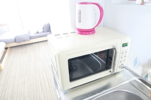 A microwave oven with a digital display, a kettle, and a small table with a tray.