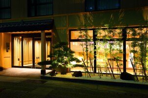 Entrada de un edificio con un jardín japonés tradicional, que incluye rocas, bambú y un sendero que conduce a las puertas.