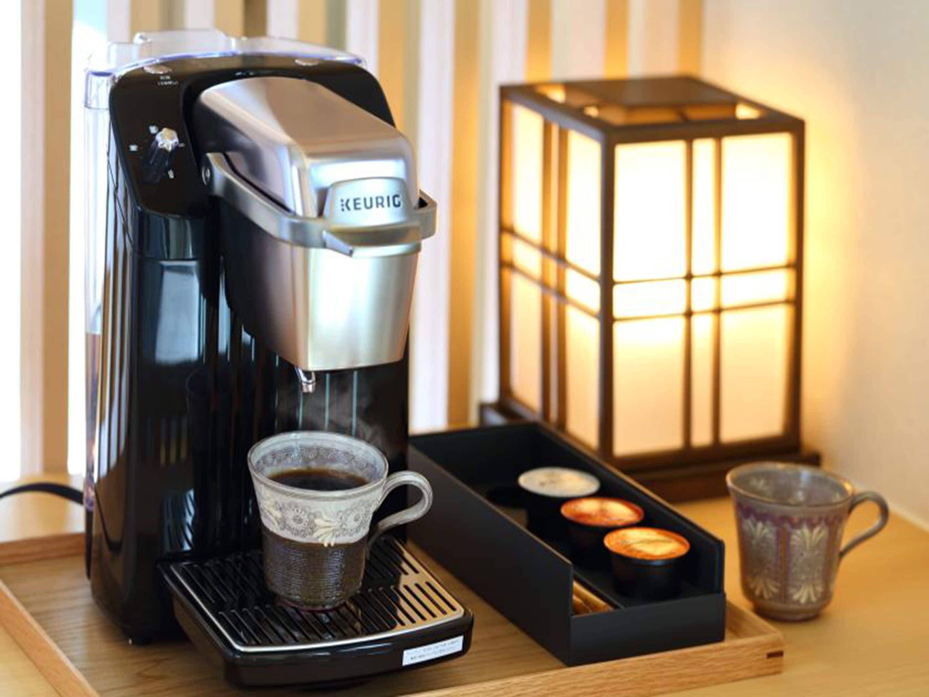 Une machine à café Keurig, une tasse de café, un plateau de dosettes de café et une bougie dans une lanterne.