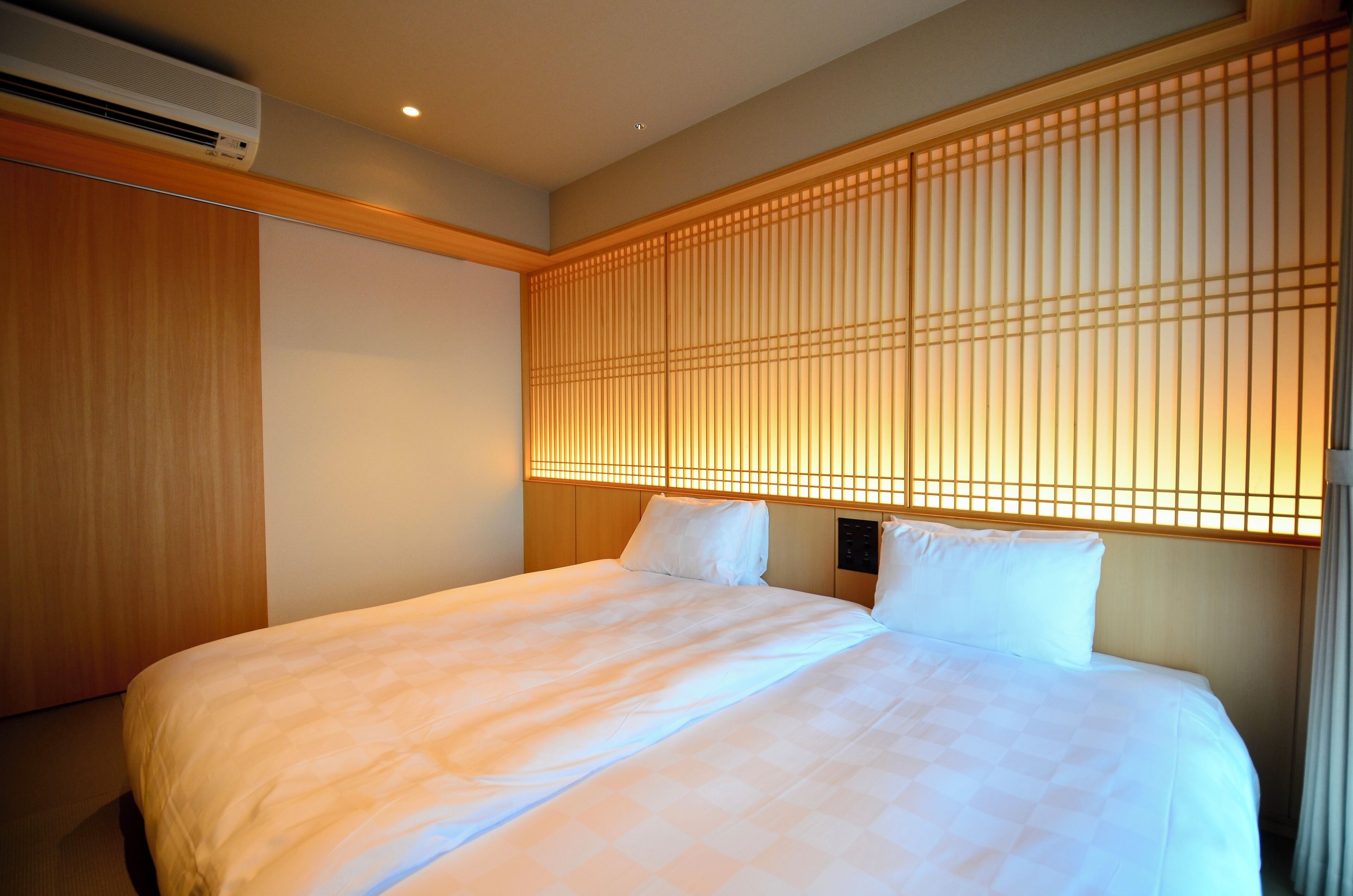 Ein Hotelzimmer mit einem Bett, einem Holzschrank und einer Wand mit vertikalen Lamellen.