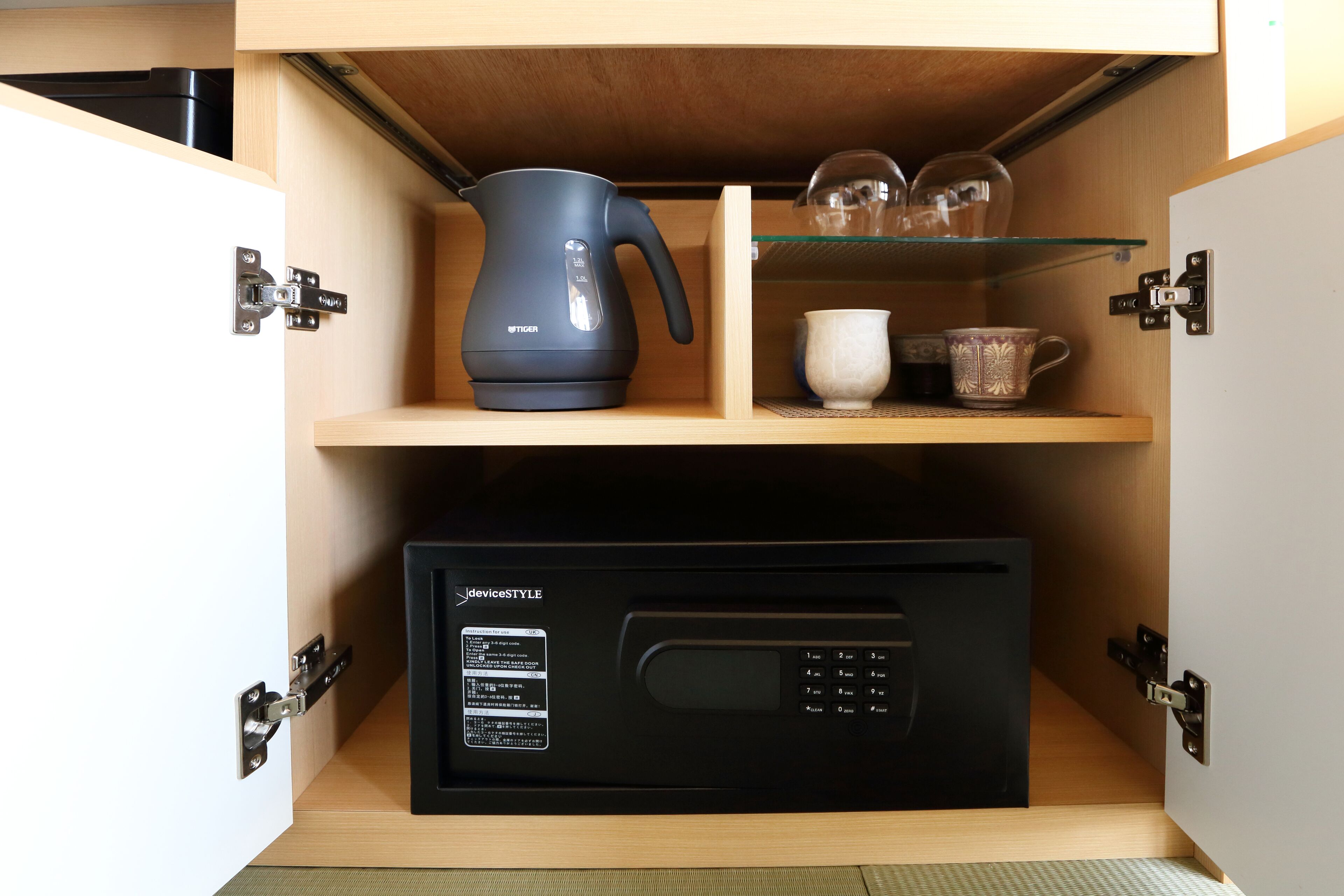 A kitchen with a black microwave, a black electric kettle, and a glass shelf with cups and a teapot.