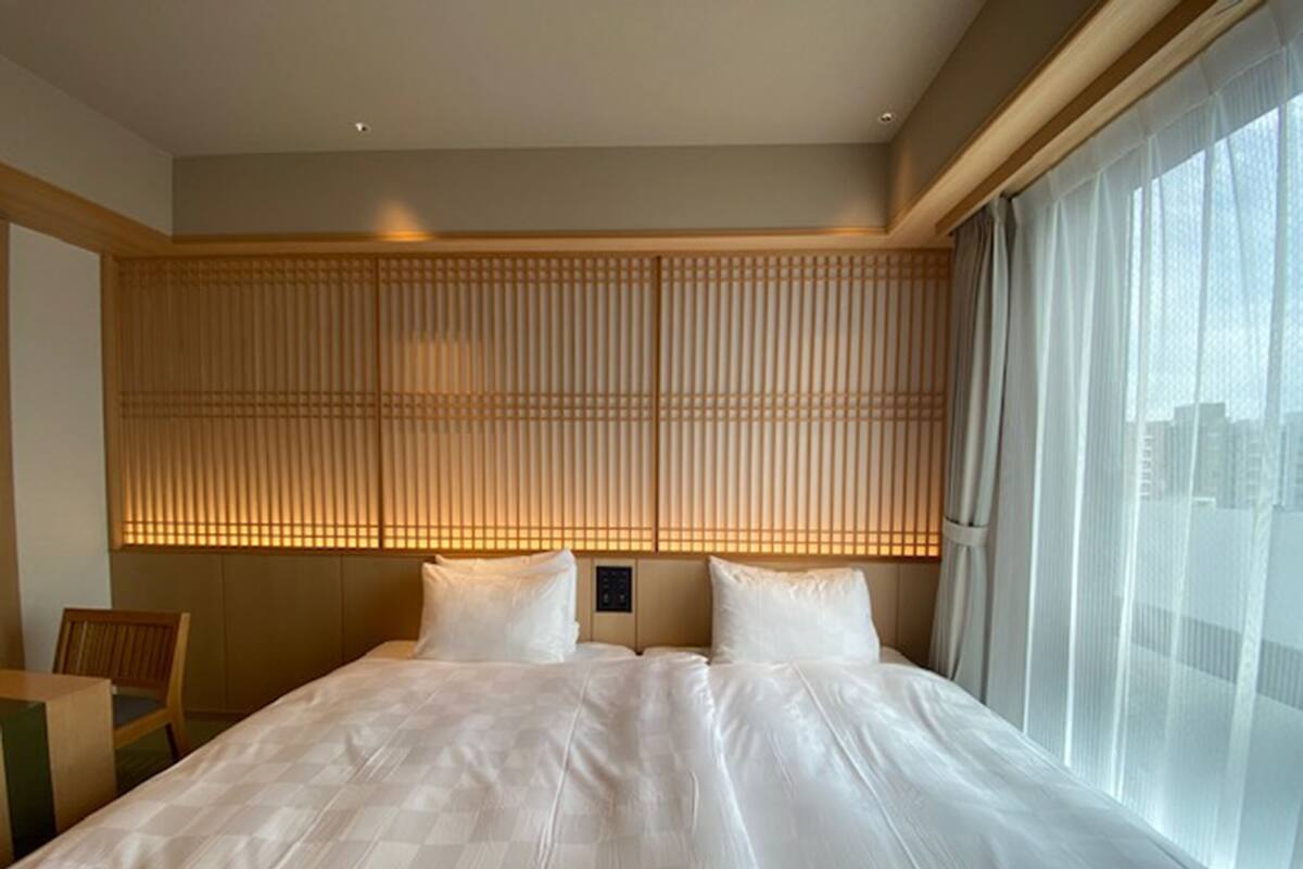 A hotel room with a large bed, a wooden headboard, a window with curtains, and a city view.
