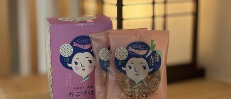 A box and a packet of Japanese snacks on a wooden surface with a traditional Japanese room in the background.