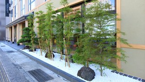 Un bâtiment à la façade moderne, une rangée de plantes de bambou et un chemin pavé de pierres.
