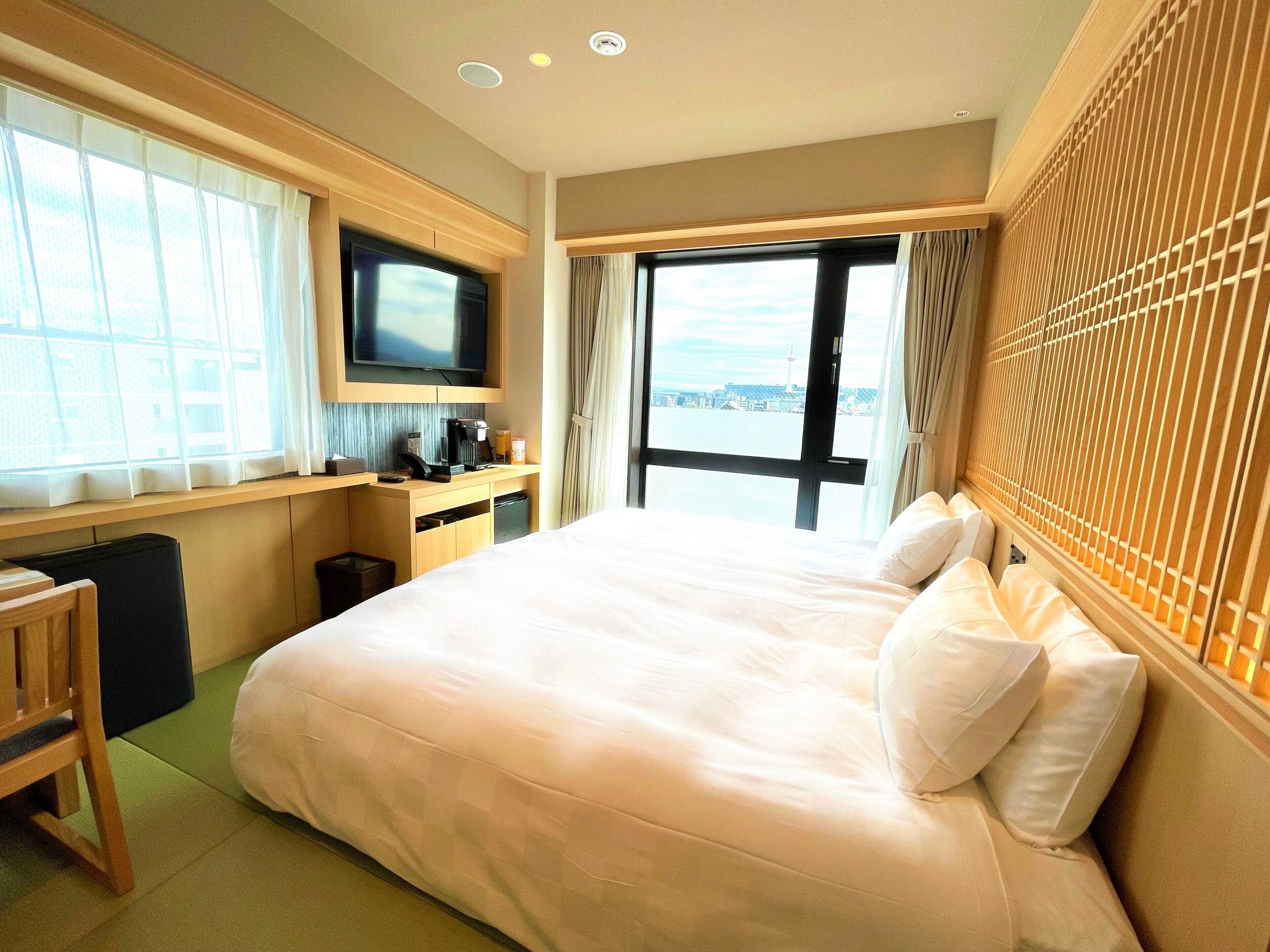 Une chambre d’hôtel avec un grand lit, une télévision, un bureau avec une machine à café et une vue sur le paysage urbain.