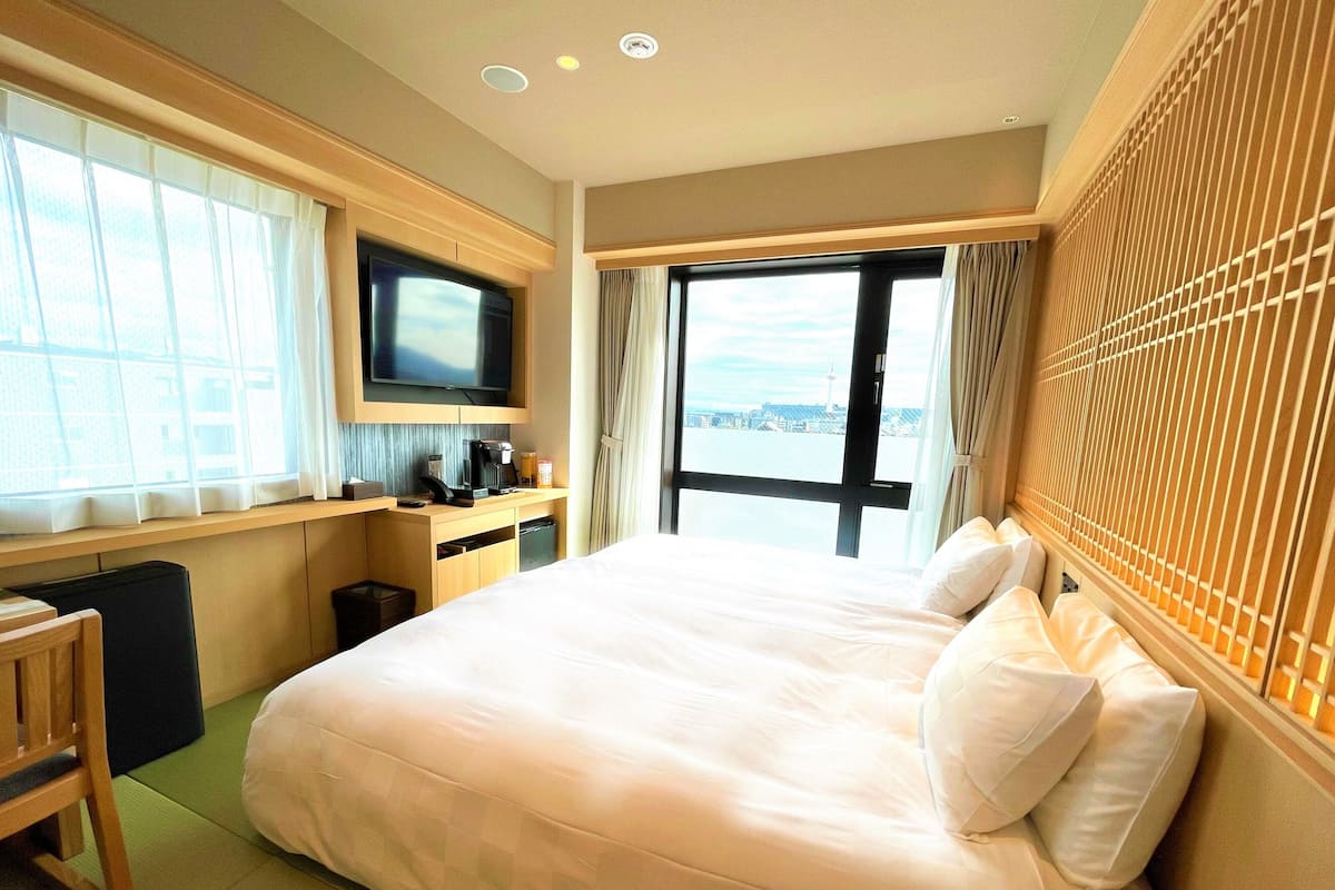 Habitación de hotel con una cama grande, televisor, escritorio con cafetera y vista a la ciudad.