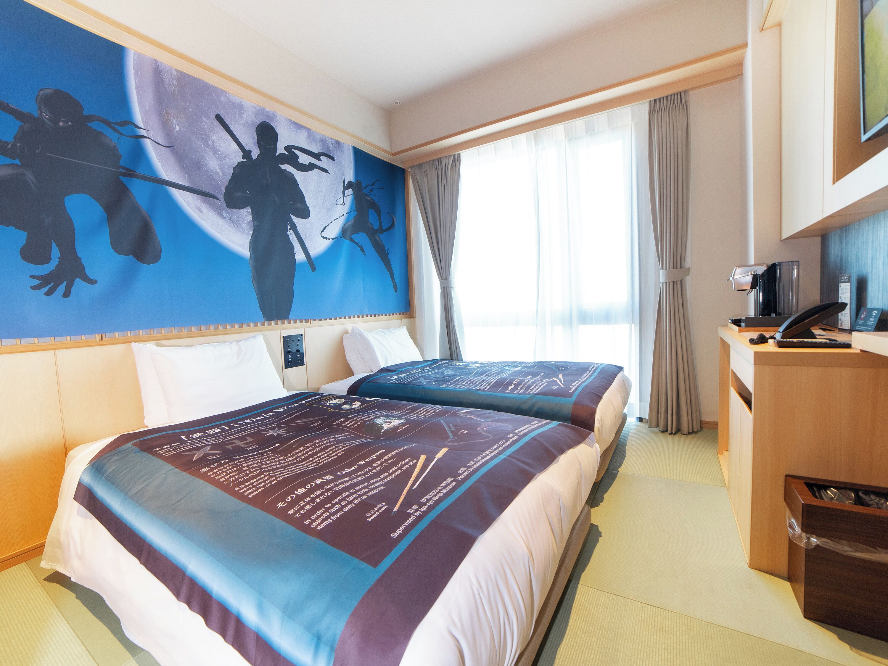 A hotel room with two beds, a desk, a coffee machine, and a large wall mural.