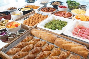 Ein reichhaltiges Buffet mit verschiedenen Speisen, darunter Croissants, Salaten und Fleisch.