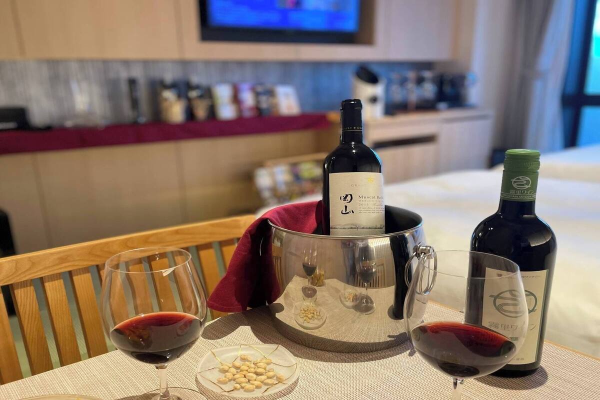A hotel room with a dining table set with wine glasses, a bottle of wine, and a plate of peanuts.
