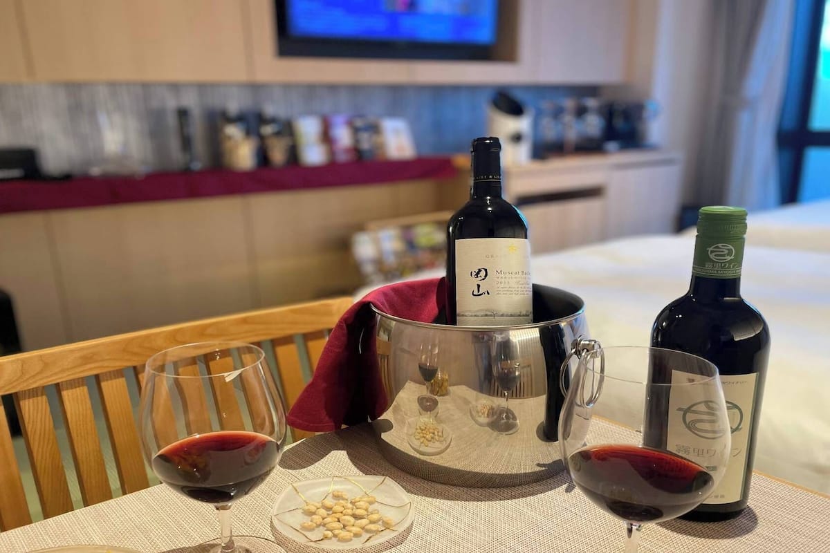 Habitación de hotel con una mesa de comedor dispuesta con copas de vino, una botella de vino y un plato de cacahuates.