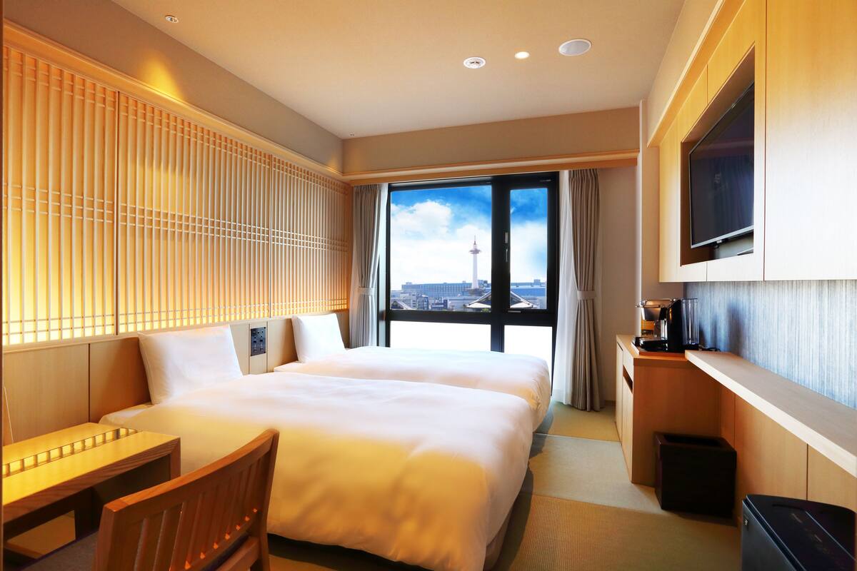 A hotel room with a large bed, a desk, a TV, and a view of a tower.