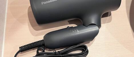 Egy Panasonic hajszárító, amelynek a tápkábele és a csatlakozója egy fa felületen található.