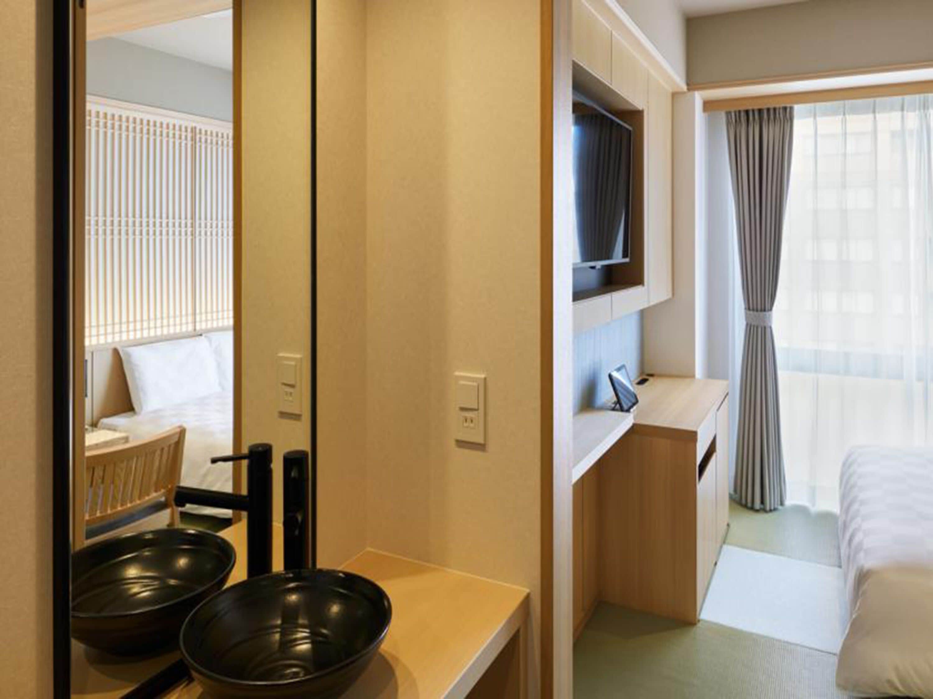 A hotel room with a bed, a TV mounted above the dresser, a mirror, and a window with curtains.