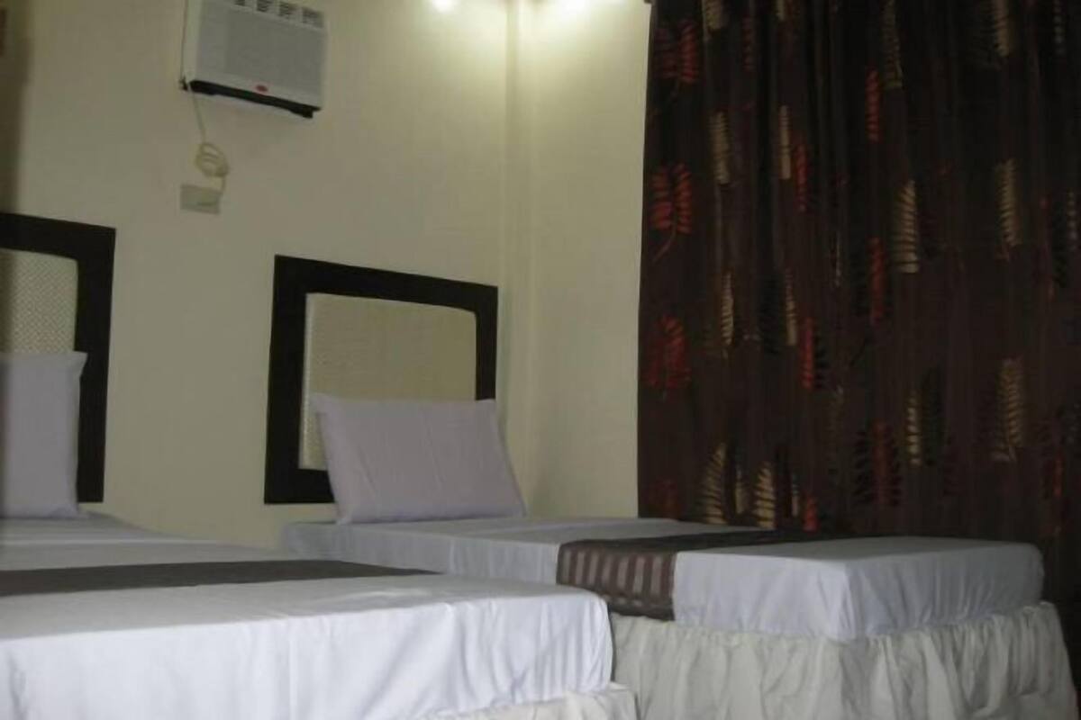 A hotel room with two beds, a wall-mounted air conditioner, and a patterned curtain.