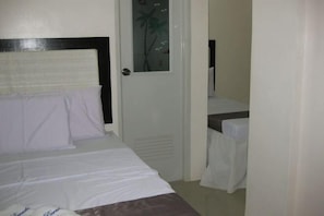 Una habitación de hotel con una cama, una puerta con panel de vidrio y una pequeña mesa con mantel blanco.