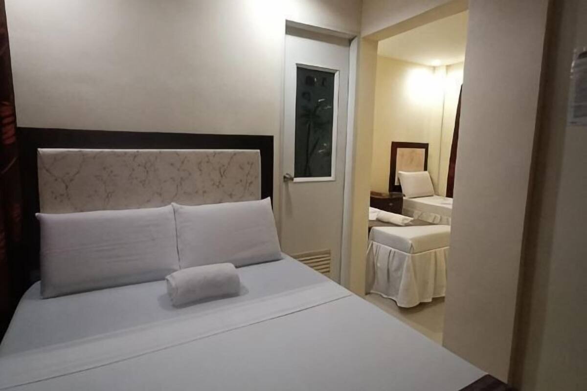 A hotel room with a bed, a door leading to a bathroom, and a small table with a chair.
