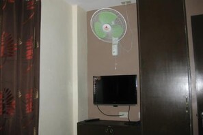 Een kamer met een tv aan de muur en een staande ventilator.