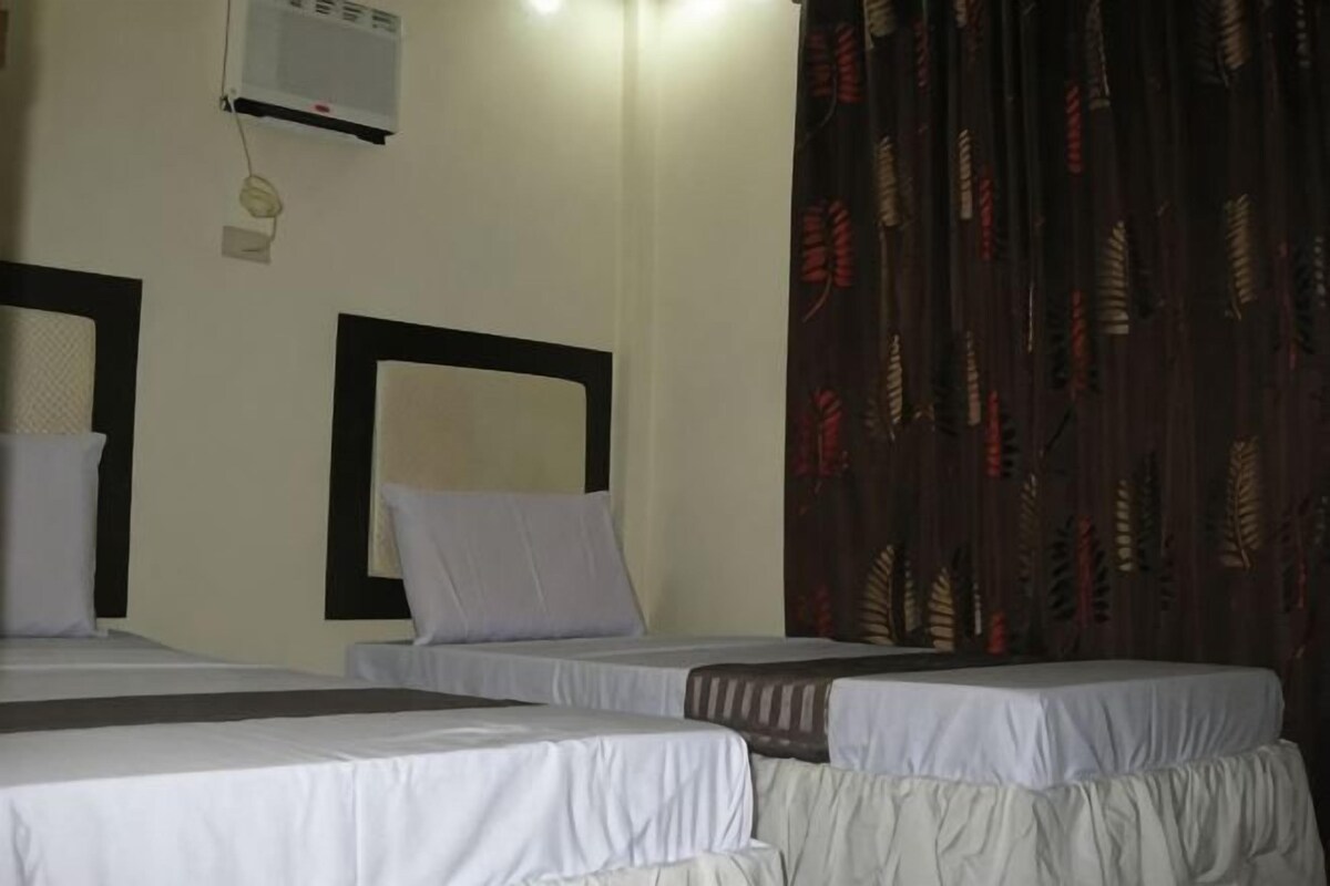 A hotel room with two beds, a wall-mounted air conditioner, and a patterned curtain.