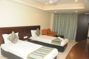 A hotel room with two beds, a wooden headboard, a small table, and a chair. - Suvarna Regency (Hassan)