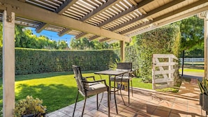 Une terrasse couverte avec une table et des chaises, une plante en pot et un portail blanc.