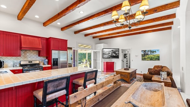 Une cuisine moderne avec des meubles de rangement rouges, un grand îlot central doté de tabourets de bar et une table en bois rustique.