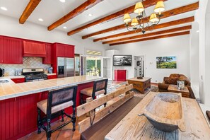 A modern kitchen with red cabinets, a large island with bar stools, and a rustic wooden table.