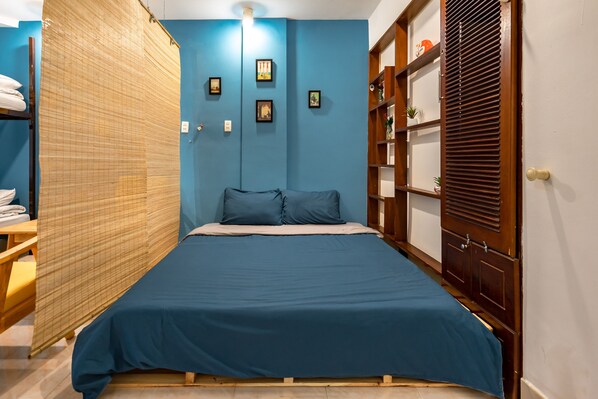 A bedroom with a bed, a wooden wardrobe, and a shelf with decorative items.