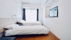 A hotel room with two beds, a TV mounted on the wall, and a window with curtains. - Hostel 758 Nagoya3A (Nagoya)