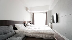 A hotel room with a bed, a sofa, a bedside table with a lamp, and a TV mounted on the wall.