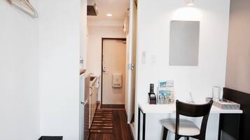 A modern hotel room with a wooden floor, a dining area with a table and chairs, a small kitchen, and a hallway leading to another room.