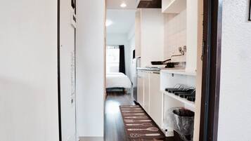 A narrow hallway leading to a bedroom with a bed and a kitchenette.