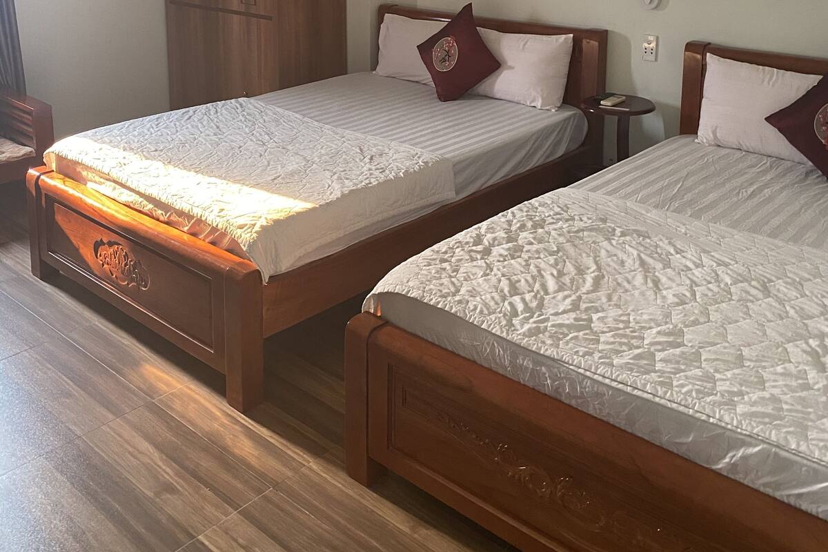 Dos camas de madera con ropa de cama blanca, un armario de madera y una mesita de noche con lámpara.