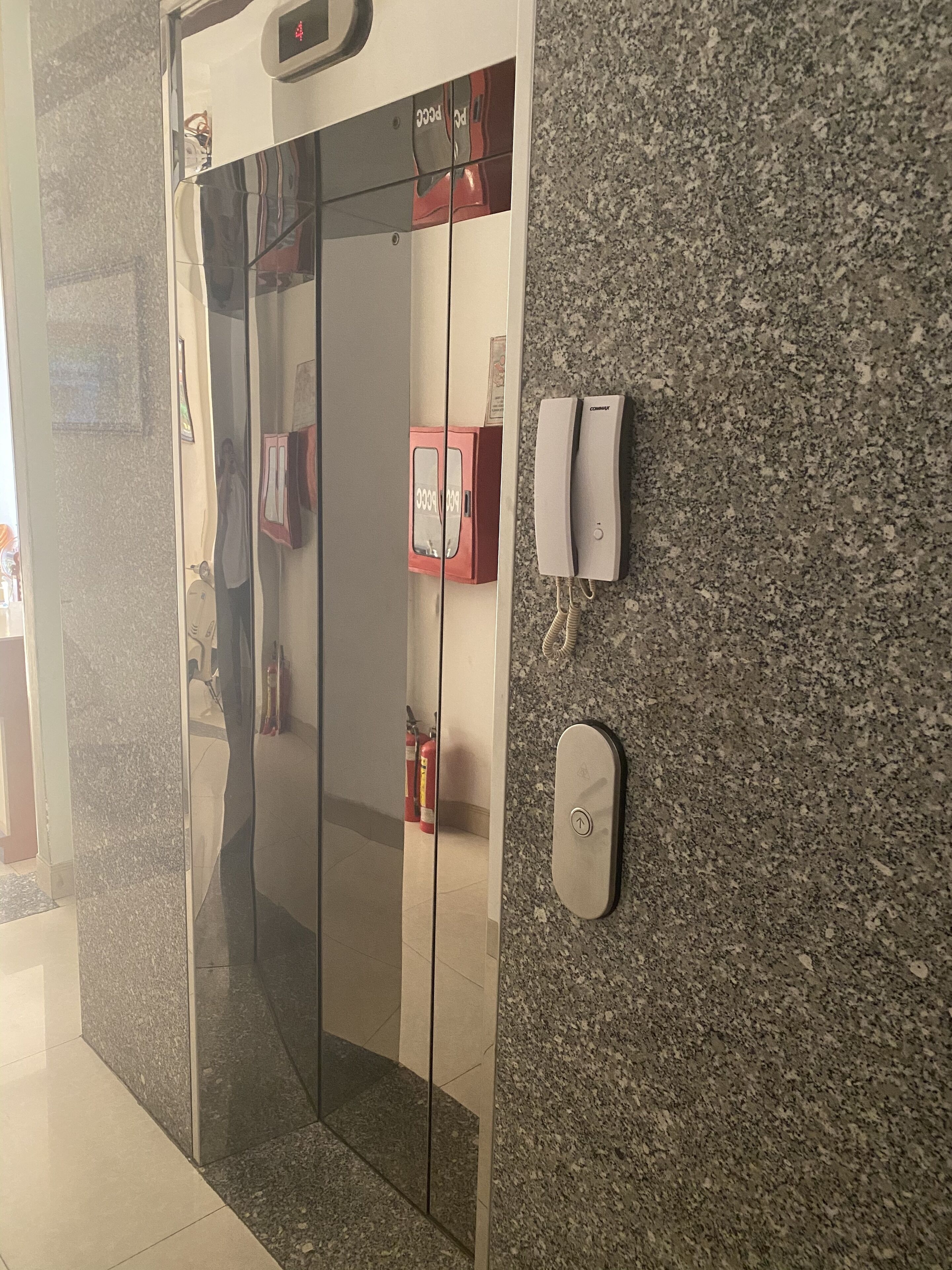 A modern elevator with a digital display, a fire alarm, and a telephone on the wall.