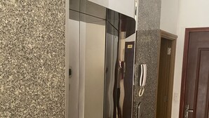 Un ascenseur moderne doté d’un écran numérique, d’un bouton d’urgence rouge et d’une porte portant le numéro 101.