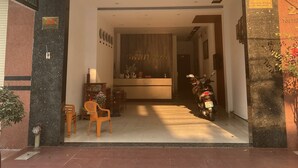 L’entrée d’un hôtel, avec un comptoir d’accueil, une moto garée à l’extérieur et une enseigne indiquant le nom et l’adresse de l’hôtel.