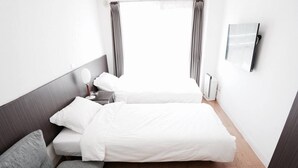 Een hotelkamer met een bed, een grijze bank, een nachtkastje en een aan de muur bevestigde televisie.