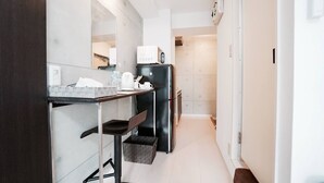 A narrow kitchen with a refrigerator, a small bar stool, and a countertop with a kettle and cups. - Hostel 758 Nagoya2S (Nagoya)