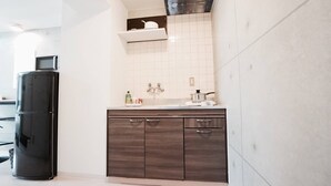 A modern kitchen with a built-in stove, a microwave, and a dark wooden cabinet with drawers. - Hostel 758 Nagoya2S (Nagoya)