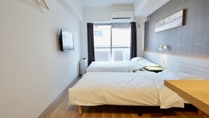 Quarto de hotel com duas camas, piso de madeira, televisão de tela plana e janela com cortinas.