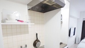 A compact kitchen with a sink, a stove, and a microwave. There is a small shelf above the sink with a pot and a kettle. - Hostel 758 Nagoya2B (Nagoya)