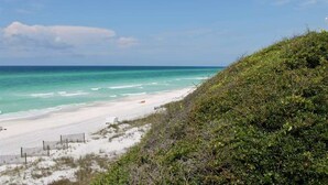 A beach with white sand, a wooden fence, and a grassy hill.