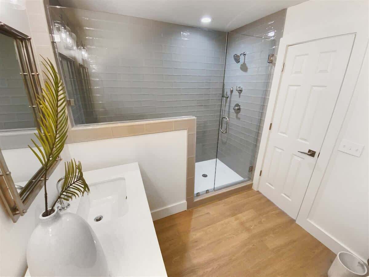 Een badkamer met een wit wastafelmeubel, een douchecabine van glas en een witte deur.
