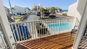 A balcony with a wooden floor, a white railing, and a view of a swimming pool and buildings.