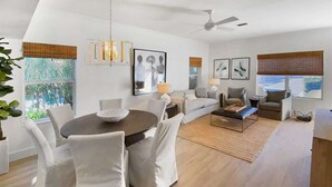 A modern living room with a round dining table, white cushioned chairs, a sofa, and a coffee table.