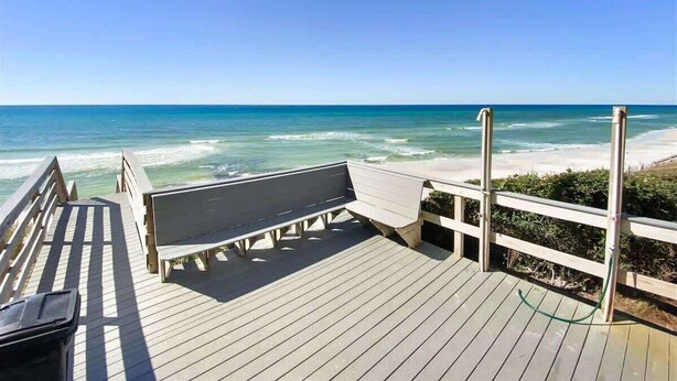 A wooden deck with a bench overlooking a beach.
