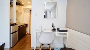 A compact hotel room with a kitchenette, a white desk, a chair, a small table, and a mirror. - Hostel 758 Nagoya3C (Nagoya)