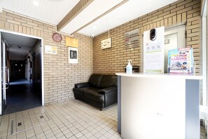 Ein Empfangsbereich mit Rezeptionstresen, einer schwarzen Ledersofa, einer Uhr und einem Schild, das 78 Zimmer für die Hostelverwaltung anzeigt.